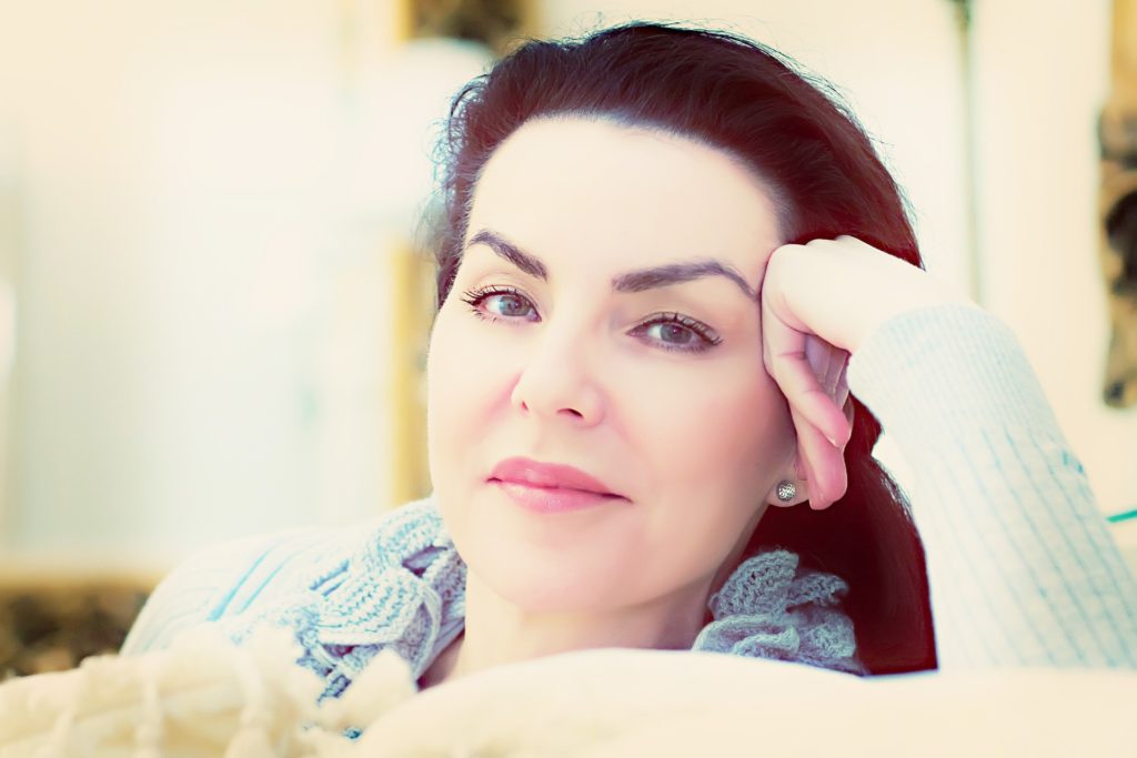 Portrait d'une femme sereine aux cheveux sombres, illustrant l'éclat de la peau et le bien-être après l'utilisation de soins anti-âge adaptés.