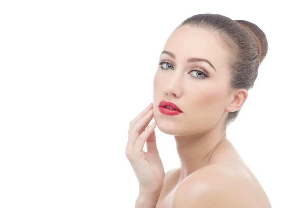 Portrait d'une femme aux yeux clos touchant son visage sereinement, illustrant la douceur et l'efficacité d'un soin exfoliant pour une peau saine.