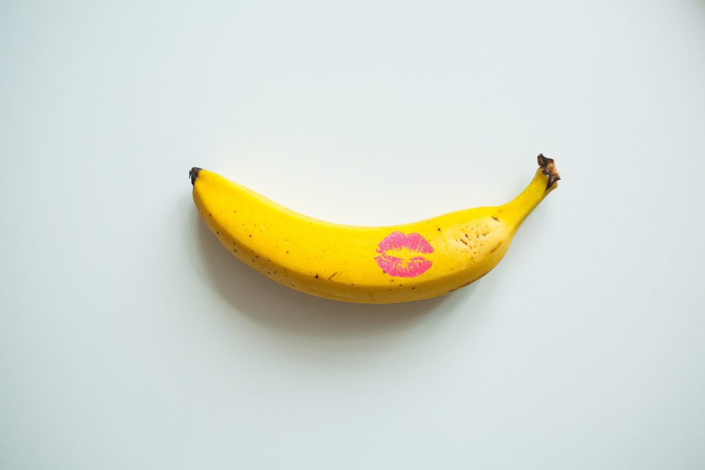 Une banane jaune sur fond blanc avec une trace de bisou au rouge à lèvres rose, symbolisant de manière créative la libido et l'énergie sexuelle.
