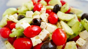 Gros plan d'une salade méditerranéenne fraîche composée de tomates cerises rouges, de concombres, d'olives noires et de cubes de fromage feta assaisonnés d'herbes.
