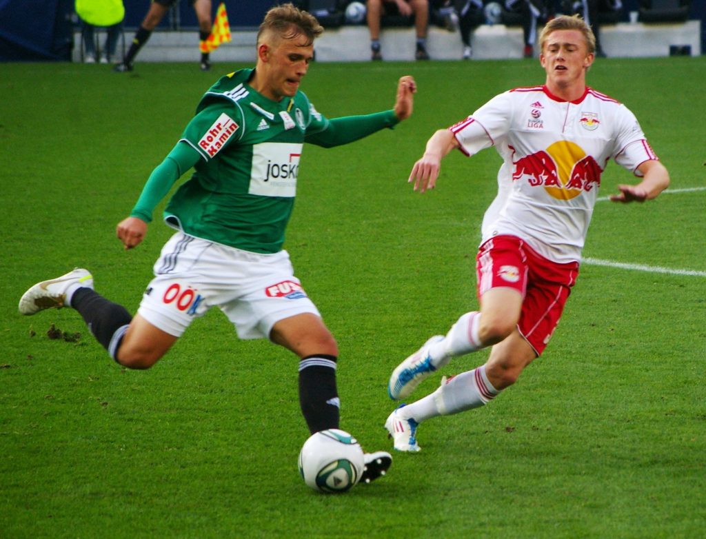 Deux footballeurs en pleine action sur un terrain de sport, illustrant l'intensité physique et le besoin de compléments nutritionnels sûrs pour les athlètes.