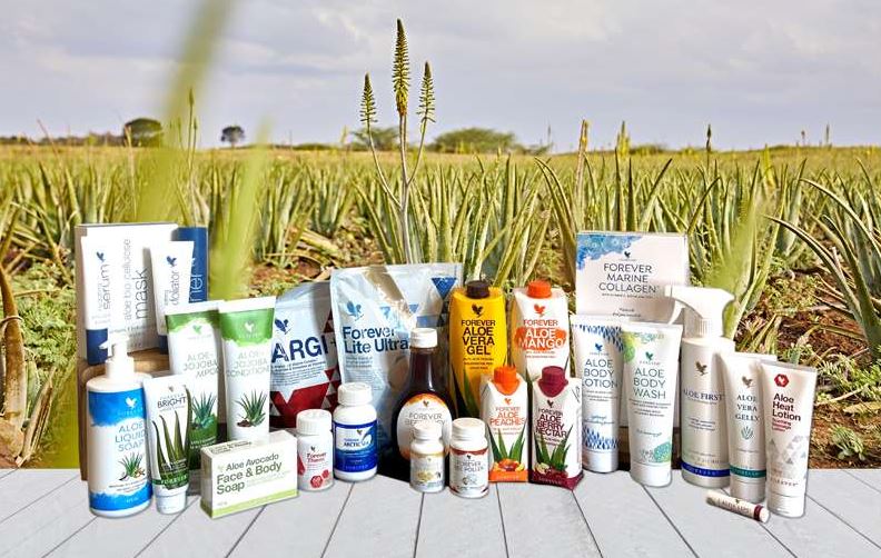 Large sélection de produits de la gamme Forever Living présentée devant un champ d'aloès, illustrant les possibilités d'économies sur l'ensemble du catalogue.