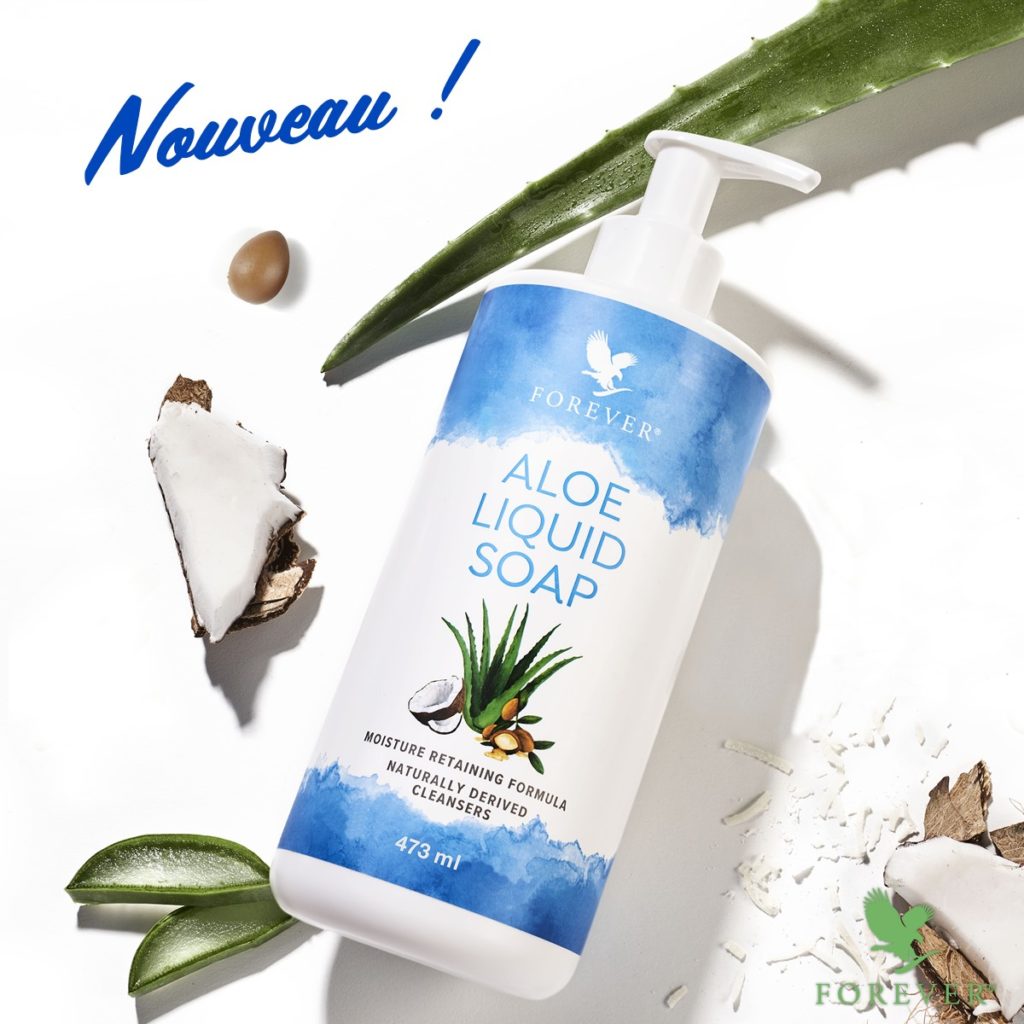 Flacon pompe de Aloe Liquid Soap de Forever entouré de morceaux de noix de coco, de feuilles d'aloès et de graines de jojoba sur fond blanc avec l'inscription "Nouveau !".