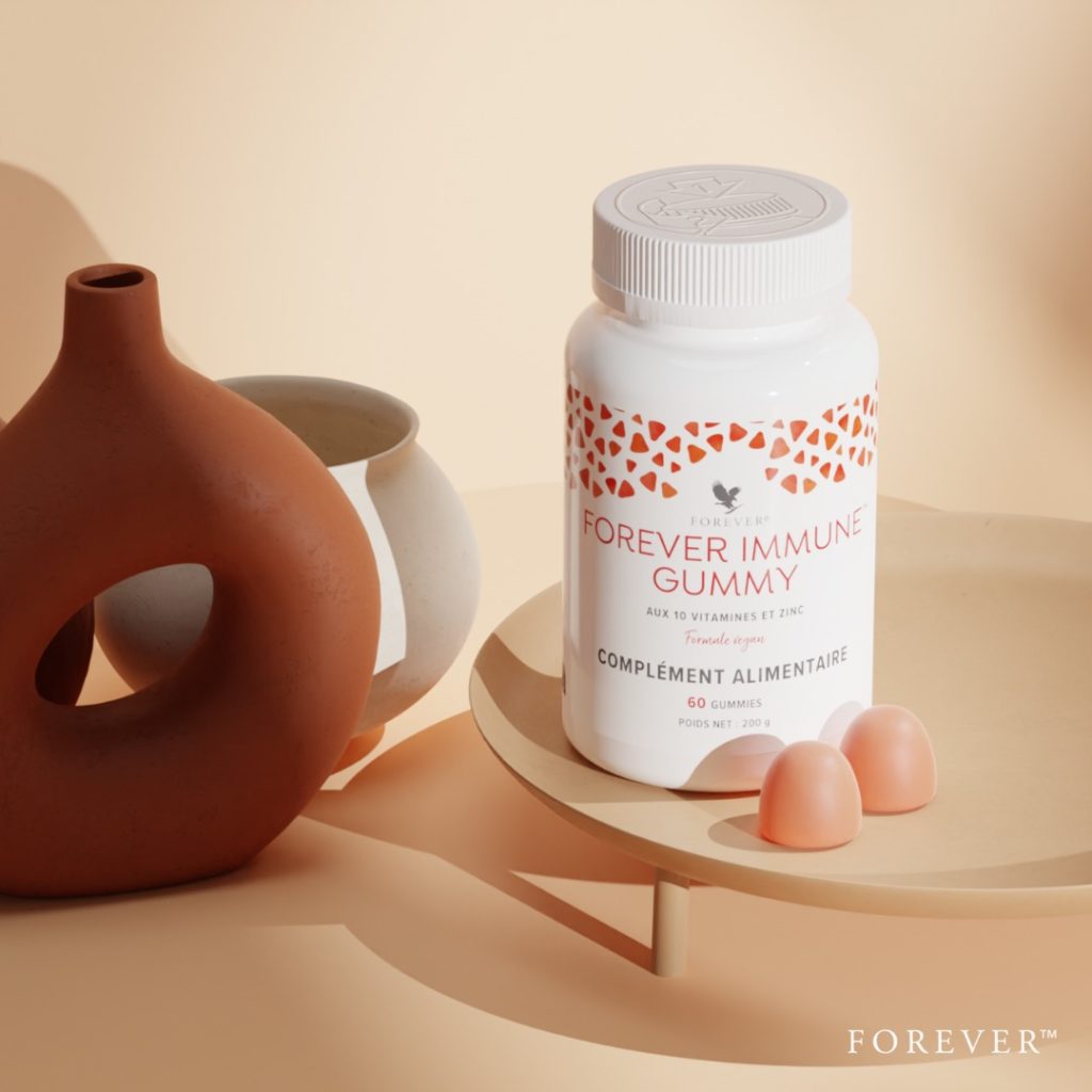 Flacon blanc de Forever Immune Gummy posé sur un plateau avec deux gummies orange à côté, accompagné de vases décoratifs sur un fond beige épuré.