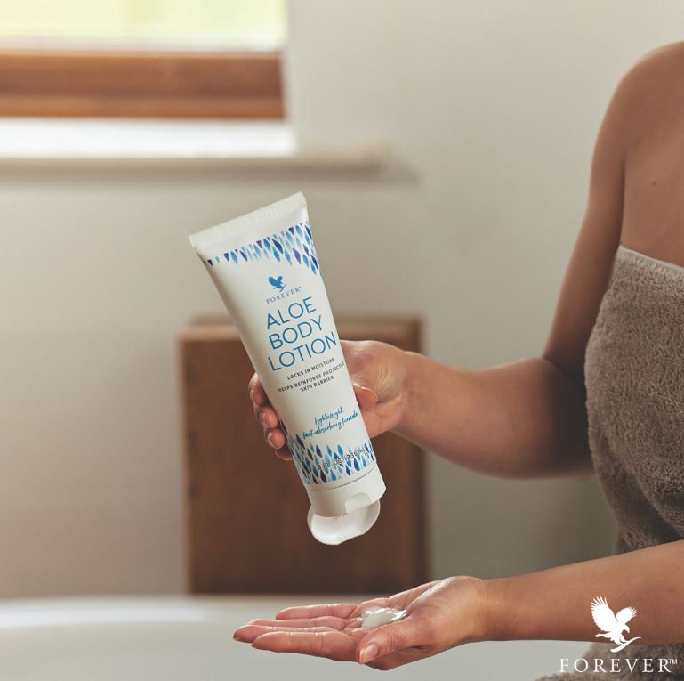 Une personne en serviette de bain versant du lait corporel Aloe Body Lotion de Forever dans le creux de sa main après la douche.