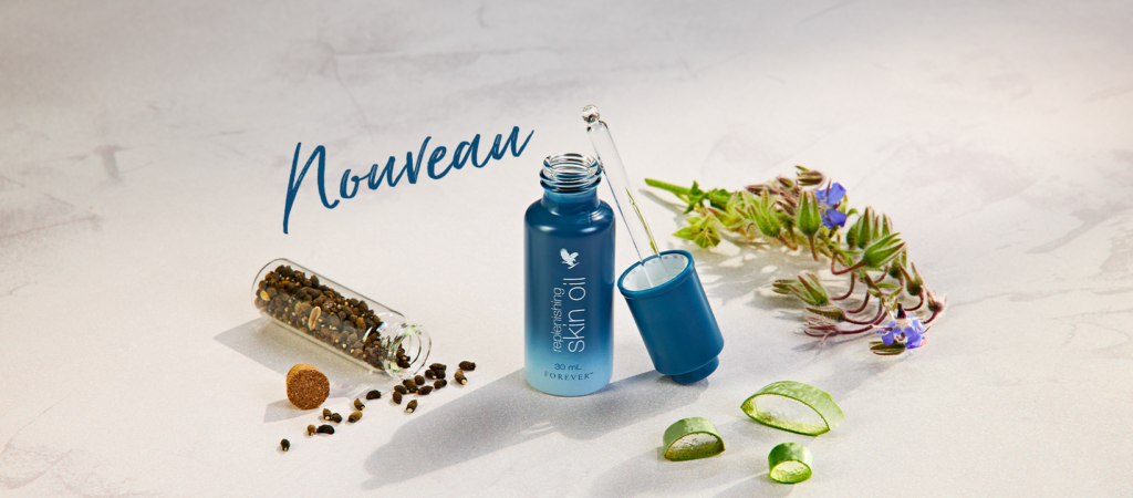 Flacon bleu dégradé de l'huile visage "Replenishing Skin Oil" de Forever Living, ouvert avec sa pipette, entouré de tranches d'aloe vera frais, de fleurs de bourrache et de graines naturelles sur un fond minéral clair.