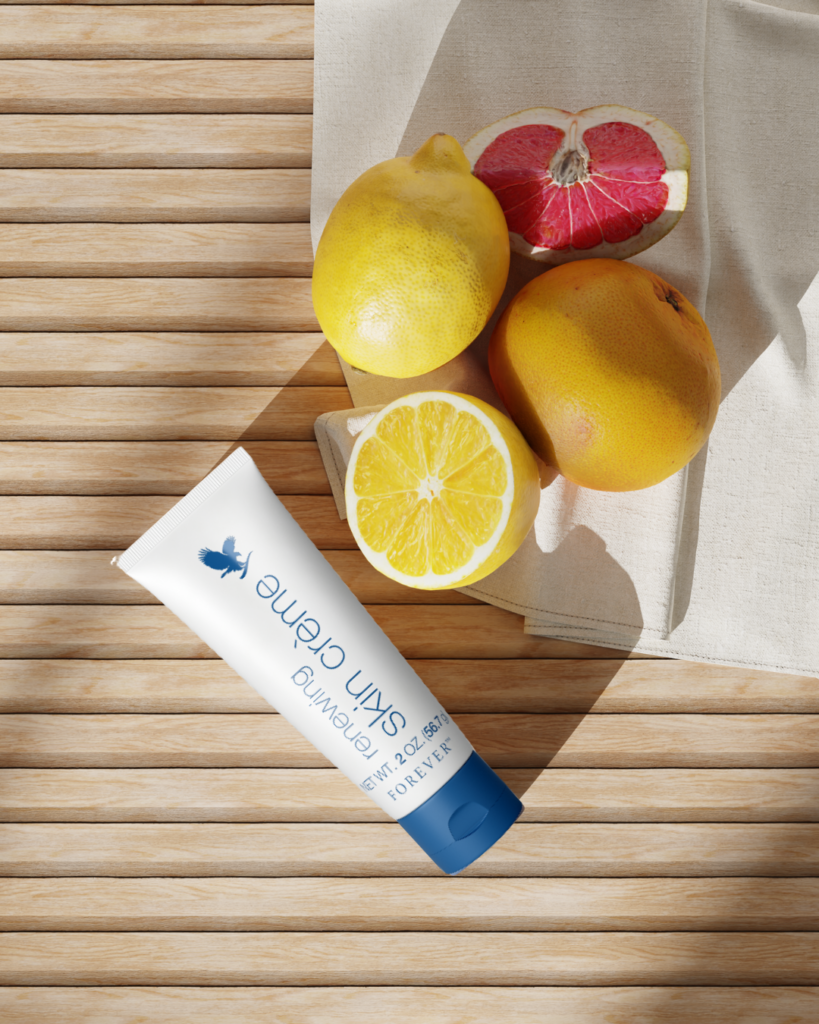 Tube de crème régénératrice Forever posé sur une table en bois à côté de citrons et d'un pamplemousse rose coupés.