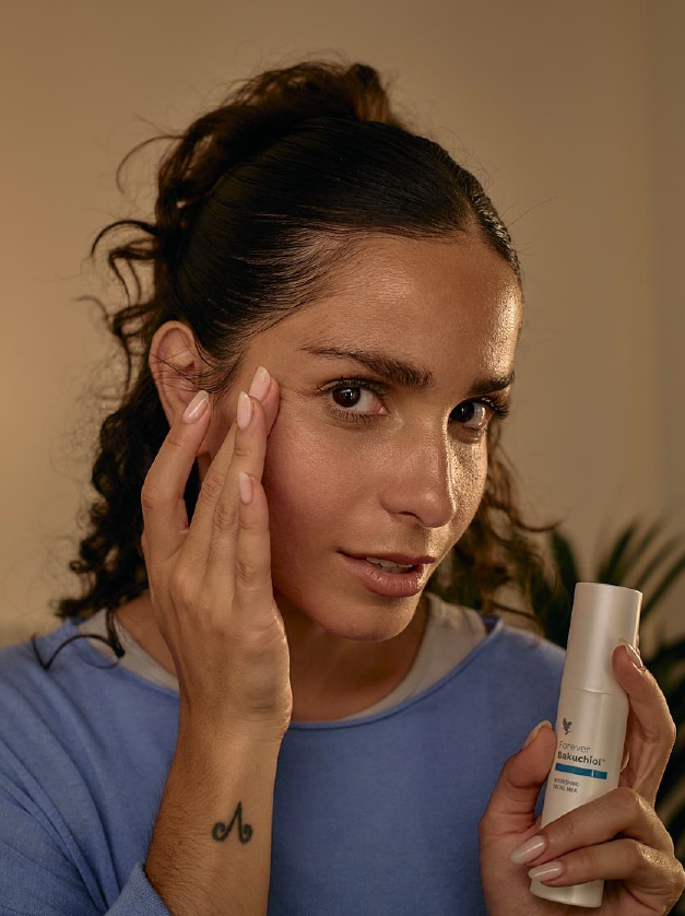 Femme appliquant du bout des doigts le Forever Bakuchiol Nourishing Facial Milk sur son visage, tenant le flacon dans l'autre main, dans une ambiance de soin du soir.