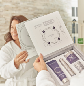 Femme en peignoir blanc découvrant le coffret Infinite by Forever contenant le démaquillant, le sérum, la crème et le complexe raffermissant.