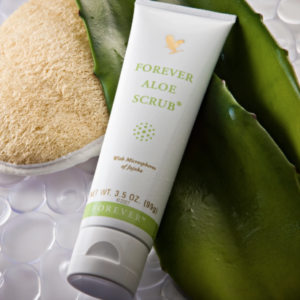 Tube de Forever Aloe Scrub posé sur des feuilles d'aloe vera fraîches avec une éponge loofah sur fond de bulles d'eau.