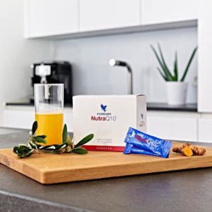 Boîte de Forever Nutra Q10 sur une table de cuisine avec un verre de jus d'Aloe Vera pour la vitalité.