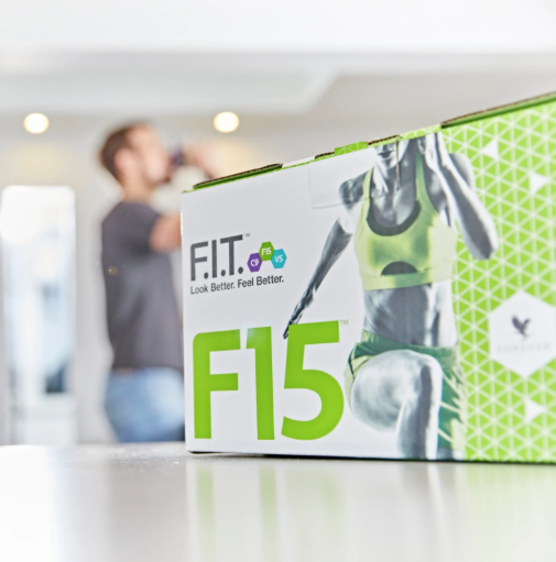 Coffret du programme Forever F15 sur une table avec un homme qui s'hydrate en arrière-plan.